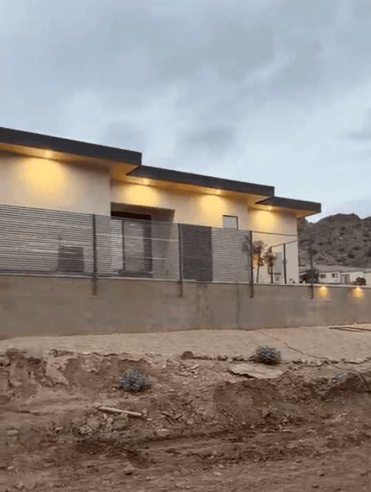 Completed horizontal steel slat privacy fence installed above a retaining wall at a modern desert home.