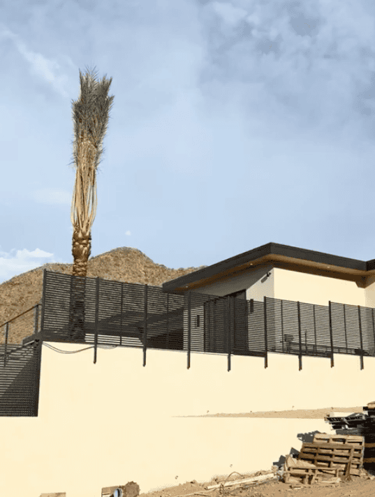 Horizontal steel slat privacy fence wrapping around the corner of an elevated modern desert home.