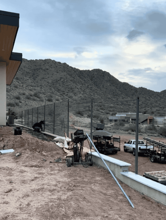 Horizontal steel slat privacy fence being installed along a retaining wall at a desert property.