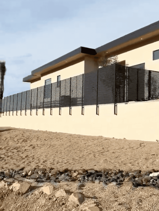 Long horizontal steel slat privacy fence installed above a retaining wall at a modern desert home.