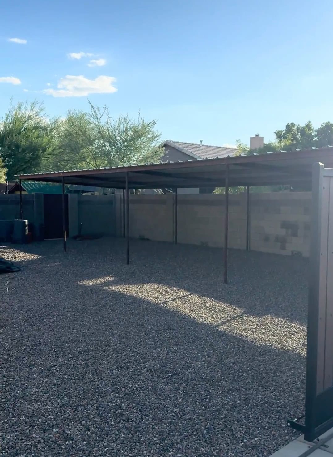 Wide view of a completed Mobile METAL Medics pipe shade structure with PBR metal roofing over a gravel outdoor area.