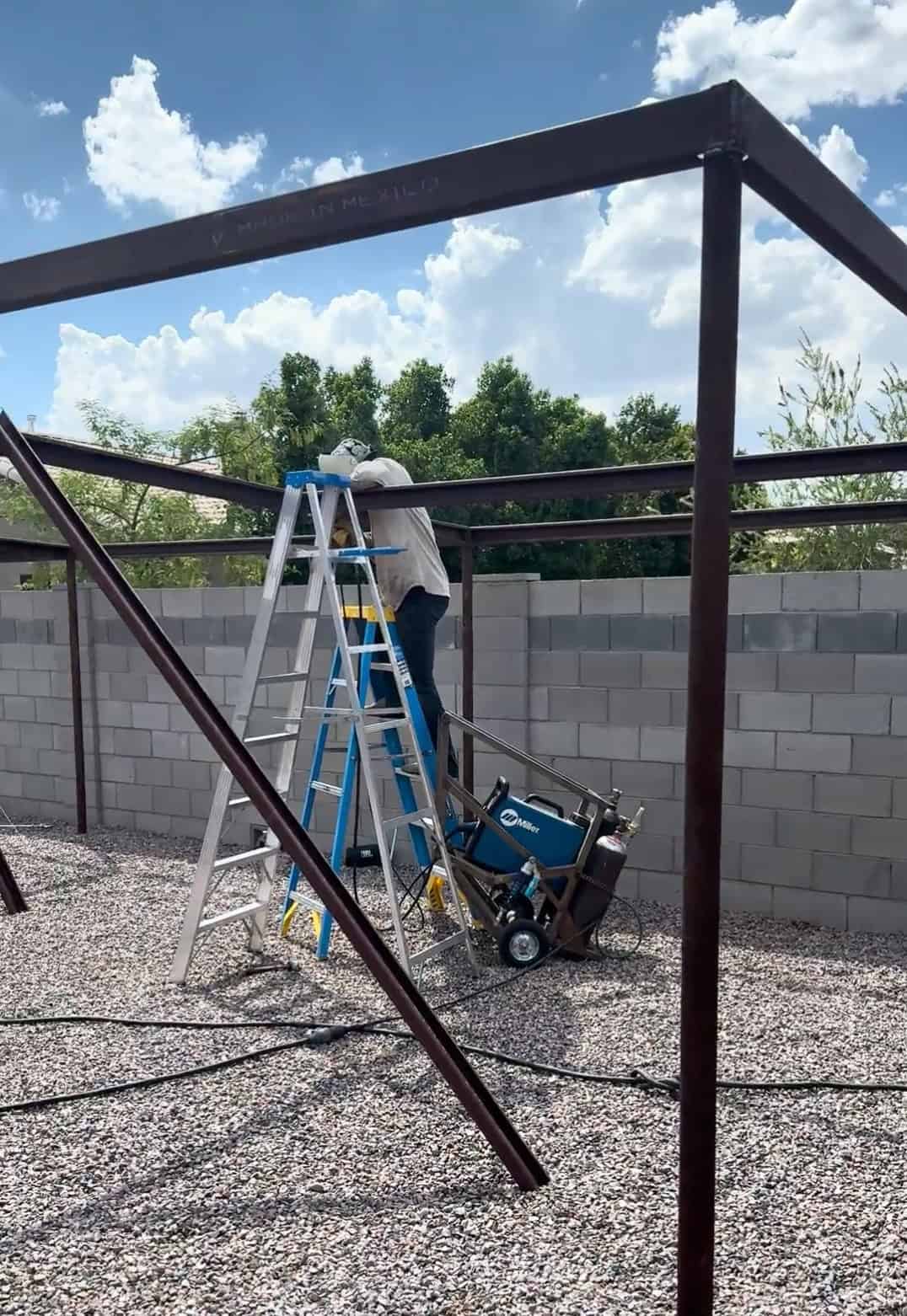 Mobile METAL Medics fabricating the upper frame of a custom pipe shade structure on site using welding equipment and ladders.