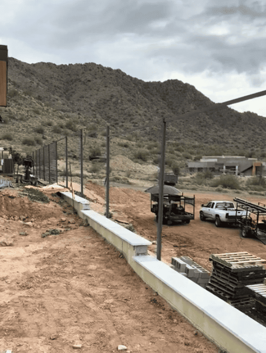 Steel slat privacy fence under construction along a raised wall at a desert home.